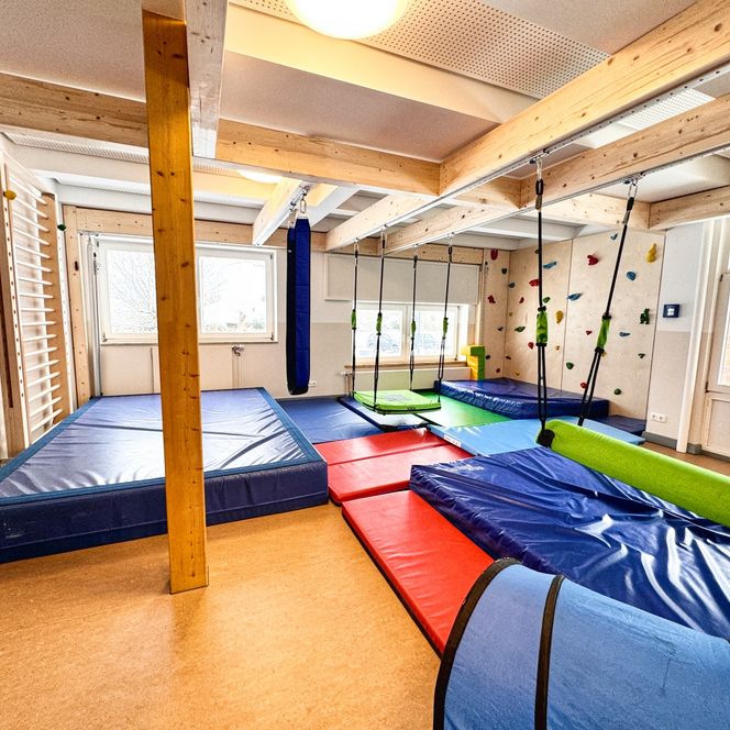 Ein Bewegungsraum im Kindergarten mit Kletterwand, Turnmatten, Hängeschaukeln und einer Sprossenwand.