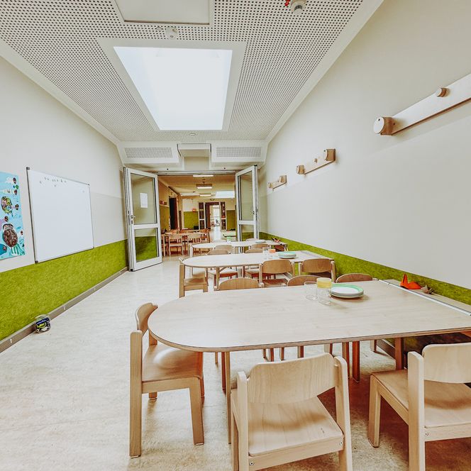 Speiseraum in der KiTa Soderstorf mit mehreren Holztischen und Kinderstühlen, an den Wänden bunte Kinderbilder und ein Whiteboard
