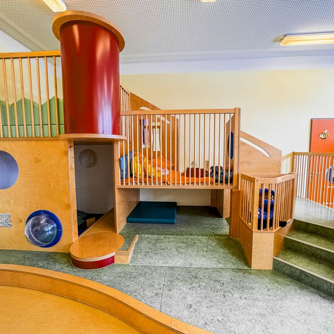 Indoor-Kletterbereich in der Kinderkrippe Amelinghausen mit Holzkonstruktion, Rutsche, Podesten und bunten Kissen