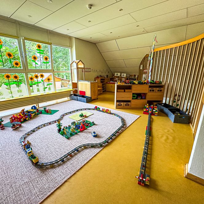 Bauecke im Kindergarten Oldendorf/Luhe mit LEGO-Eisenbahn, Spielsteinen und großen Fenstern mit Sonnenblumen-Dekoration.