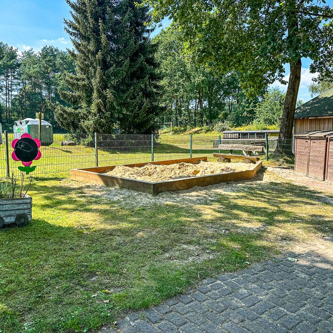 Rechteckiger Sandkasten mit umliegenden Sitzmöglichkeiten im Außengelände des Kindergartens Oldendorf/Luhe