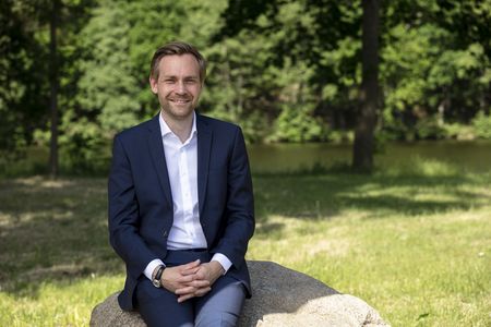 Porträt des amtierenden Samtgemeindebürgermeisters Christoph Palesch, sitzend auf einem Naturstein im Grünen vor einer Flusslandschaft.