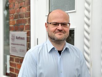 „Stephan Kaufmann, Geschäftsbereichsleiter Finanzen der Samtgemeinde Amelinghausen, steht vor dem Eingang des Rathauses und blickt freundlich in die Kamera.“