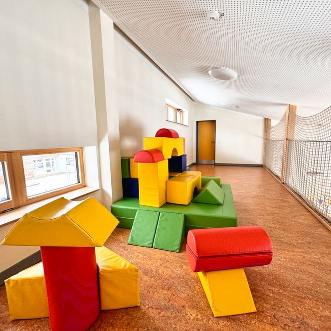 Ein Spielbereich im Kindergarten mit bunten, großen Schaumstoffbausteinen und einem Sicherheitsnetz an der Seite.