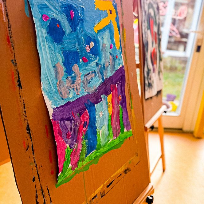 Ein farbenfrohes, mit Fingermalfarben gestaltetes Kinderbild auf einer Holzstaffelei im hellen Gruppenraum der nachschulischen Betreuung Soderstorf.