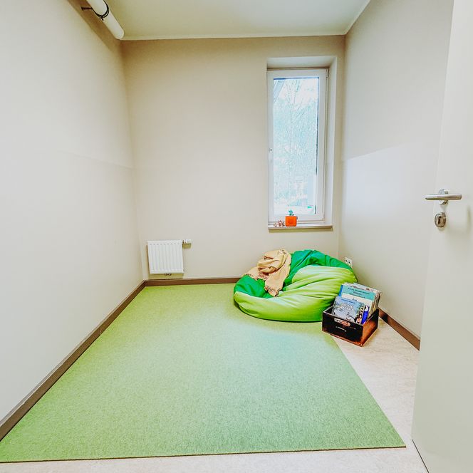 Kleiner Raum mit grünem Teppich, einem grünen Sitzsack und einer Kiste mit Büchern in der KiTa Soderstorf.