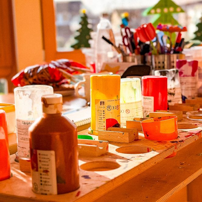 Basteltisch mit Farben, Bechern, Pinseln und Stiften für kreative Kinderprojekte.