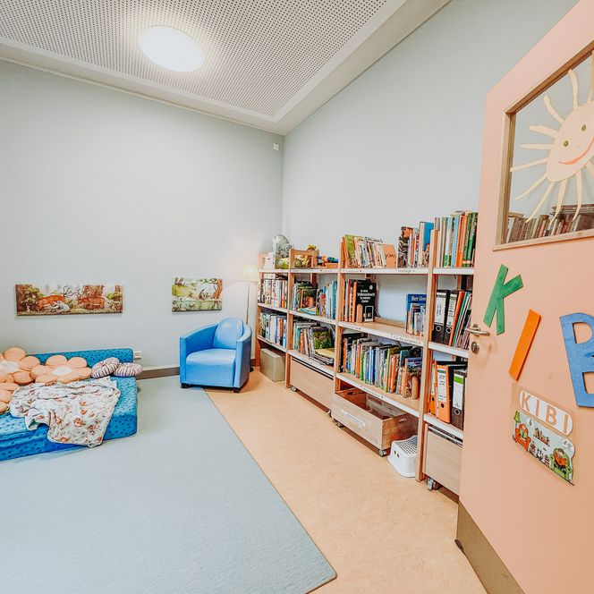 Kinderbibliothek im Kindergarten Rehlingen mit Bücherregalen, gemütlicher Leseecke mit Matratze und Sitzkissen sowie einem blauen Sessel