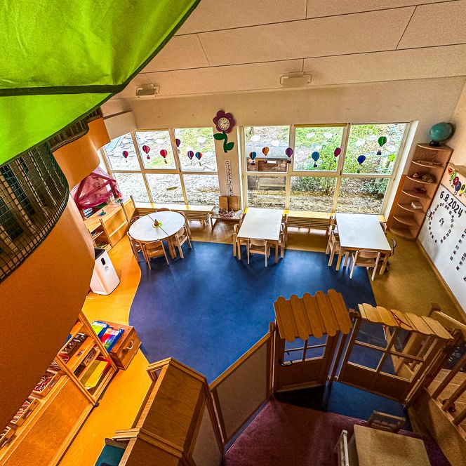 Gruppenraum im Kindergarten Oldendorf/Luhe mit runden und eckigen Tischen, großer Fensterfront und bunter Wandgestaltung.