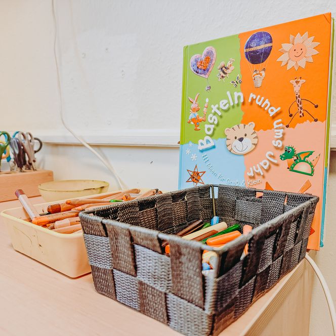 Basteltisch in der Kita Betzendorf mit Scheren, Stiften, Bastelbuch und Körben voller Mal- und Zeichenmaterialien.