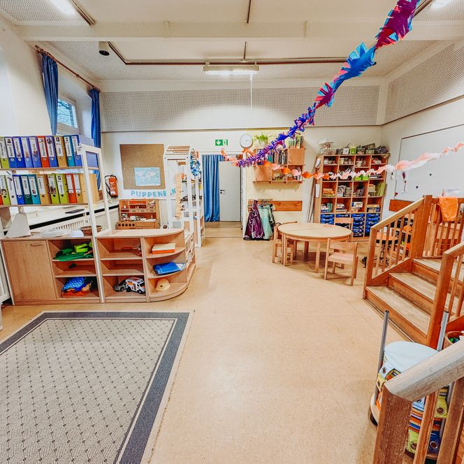 Spielbereich in der Kita Betzendorf mit Puppenecke, Regalen, Spielsachen und bunter Papierketten-Dekoration