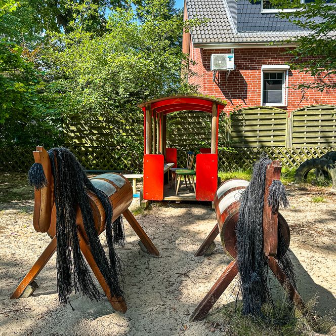 Zwei Holzspielpferde und ein roter Spielzug im Außengelände des Kindergartens Oldendorf/Luhe.
