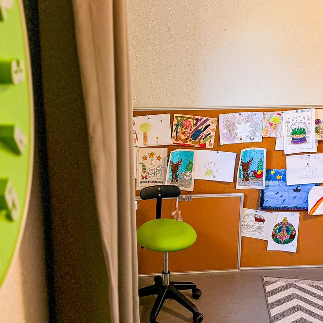 Eine Kork-Pinnwand im Jugendtreff „Be-youth“ in Amelinghausen, an der zahlreiche bunte Kinderzeichnungen und weihnachtliche Motive befestigt sind, daneben eine große grüne Wanduhr.
