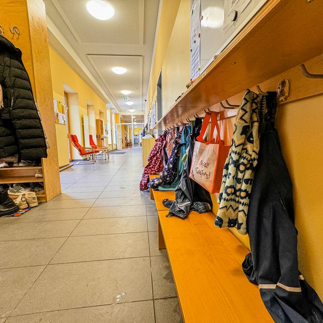 Flur der Kinderkrippe Amelinghausen mit Garderobenhaken, Kinderjacken, Schuhen und Sitzbank.