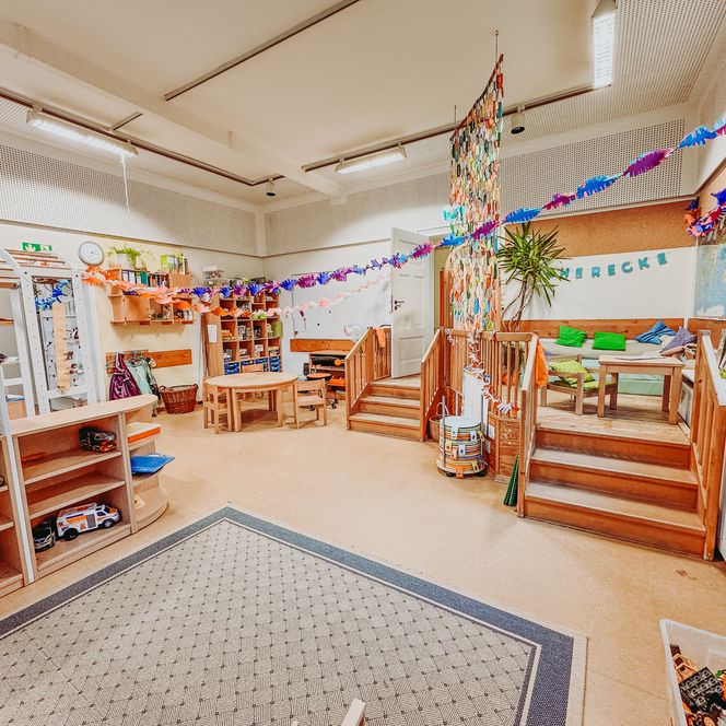 Gruppen- und Spielebereich in der Kita Betzendorf mit Tischen, Regalen voller Spielmaterial, Leseecke mit Kissen und bunter Dekoration.