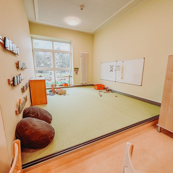 Lern- und Spielecke im Kindergarten Rehlingen mit grünem Teppich, Motorik Spielzeug und großen Fenstern mit Tiermalerei.