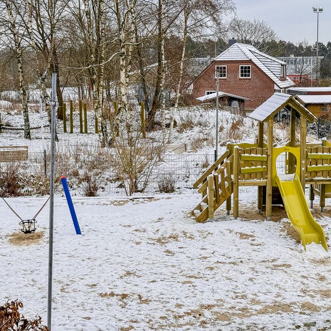 Außenspielplatz der Kinderkrippe Amelinghausen mit Klettergerüst aus Holz und gelber Rutsche im Schnee.